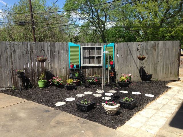 Garden corner with flowers in pots, stepping stones, and teal shutters hung on a wooden fence