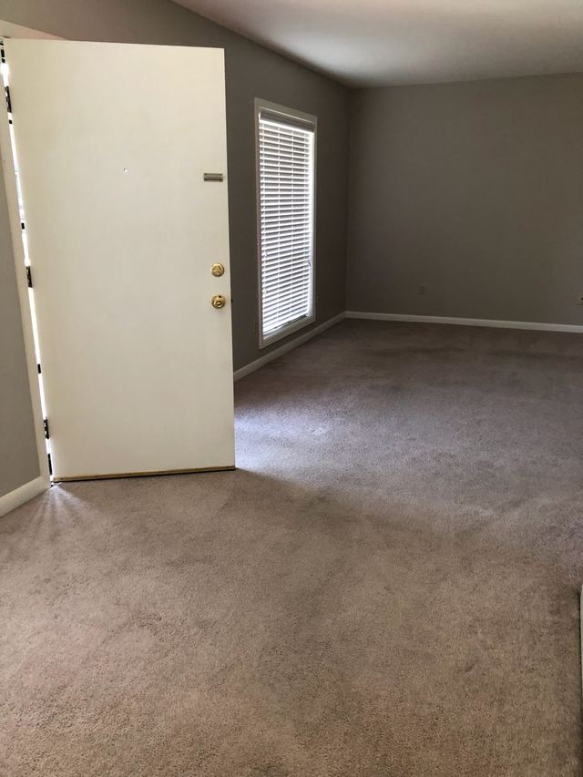 Living room in Unit 102 with gray walls, carpet, and a window with blinds