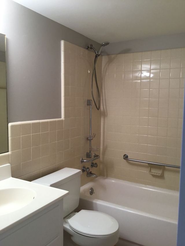 Bathroom in Unit 103 with a white tub, tiled surround, and grab bar