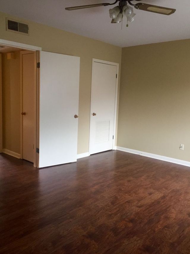 Bedroom in Unit 203 with dark wood-look flooring, closet doors, and a ceiling fan