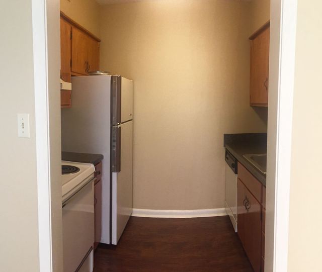 Galley kitchen in Unit 203 with white appliances and wood cabinets