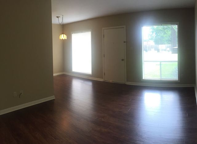 Living room in Unit 203 with dark wood-look flooring, entry door, and window