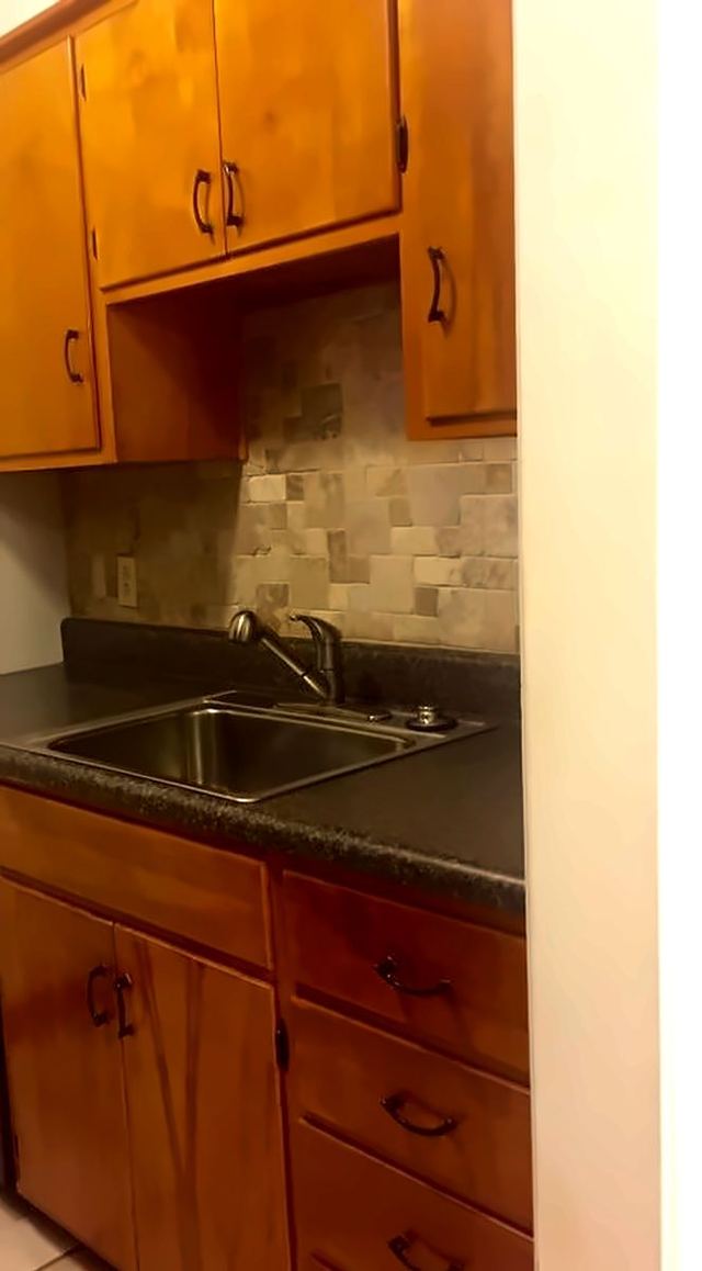 Kitchen sink area in Unit 206 with wood cabinets, stone-look backsplash, and stainless faucet