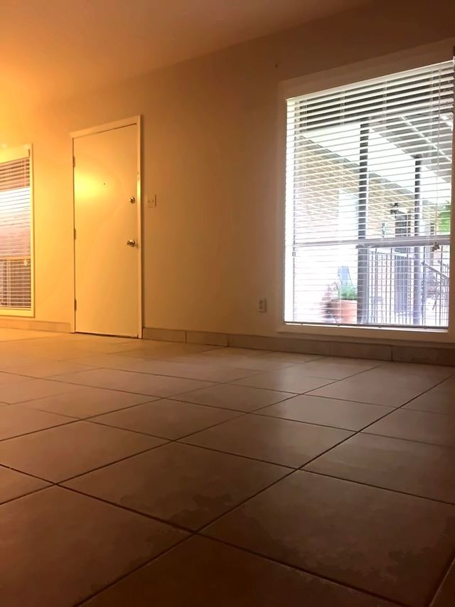 Living room in Unit 206 with light tile flooring, a window with blinds, and the entry door