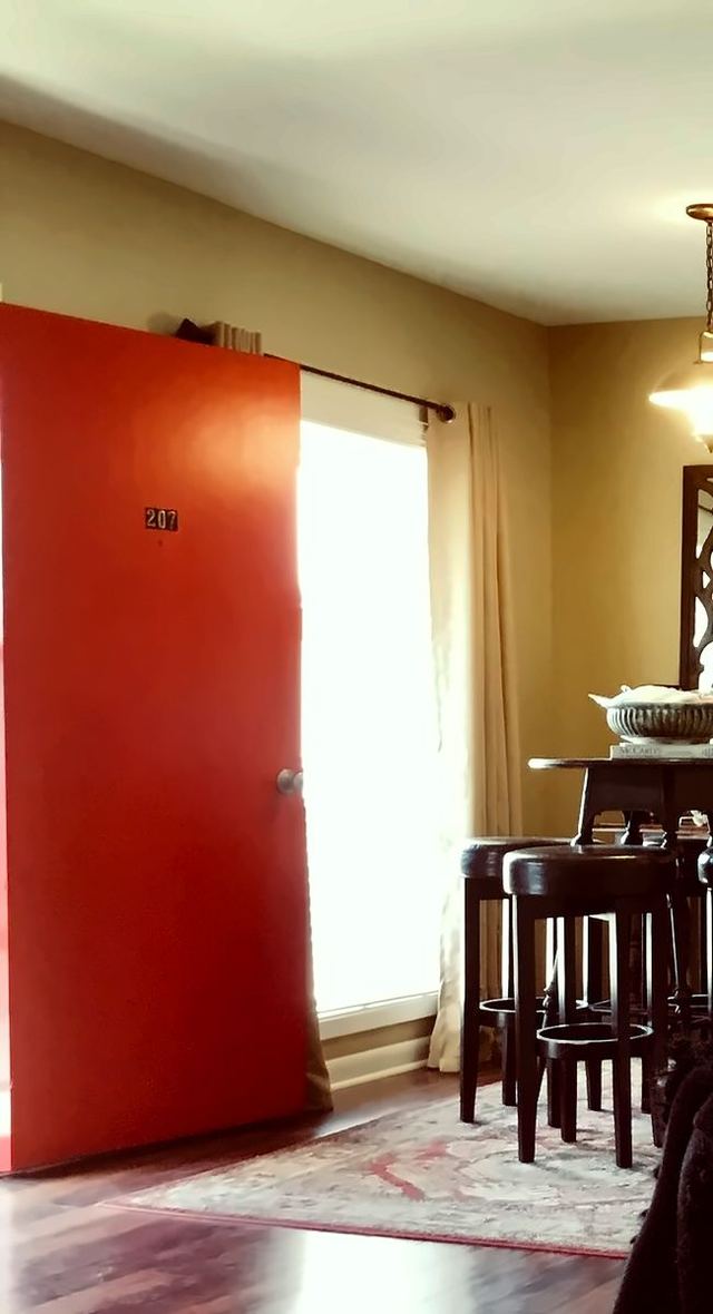 Red front door marked 207 with wood-look flooring and warm greige walls