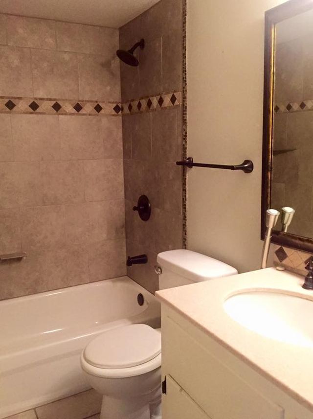 Upgraded bathroom with tiled tub surround, decorative tile border, bronze fixtures, and a framed mirror